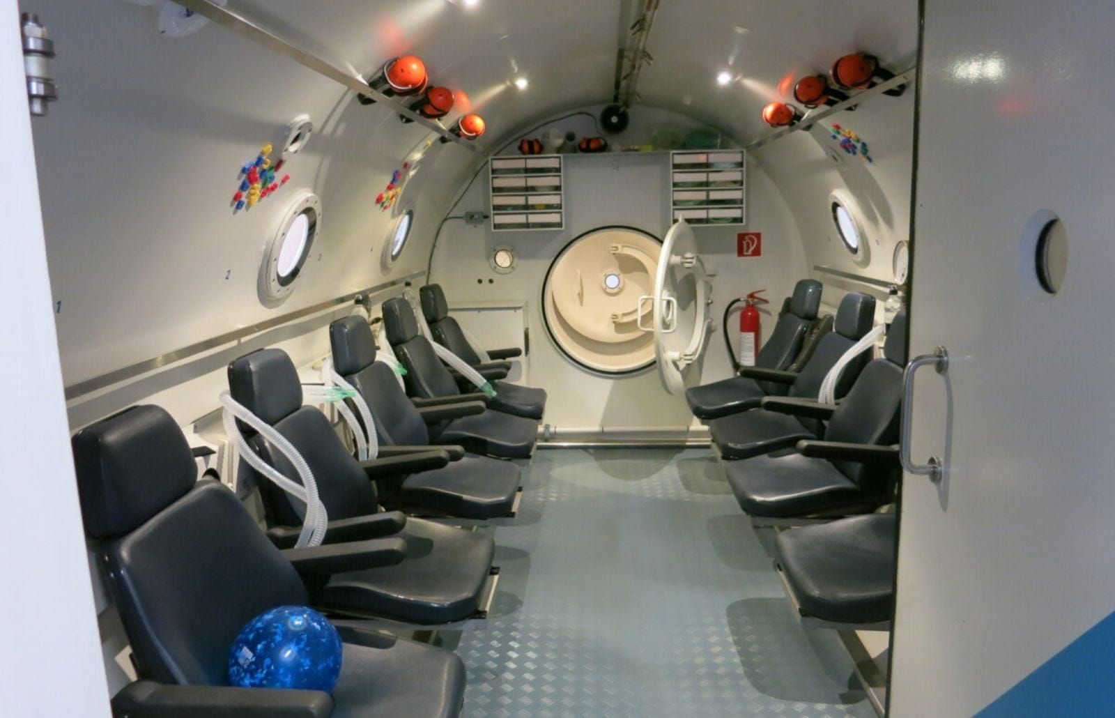 Empty hyperbaric chamber on Nusa Lembongan with rows of seats, oxygen hoses and an open hatch prepared for divers.