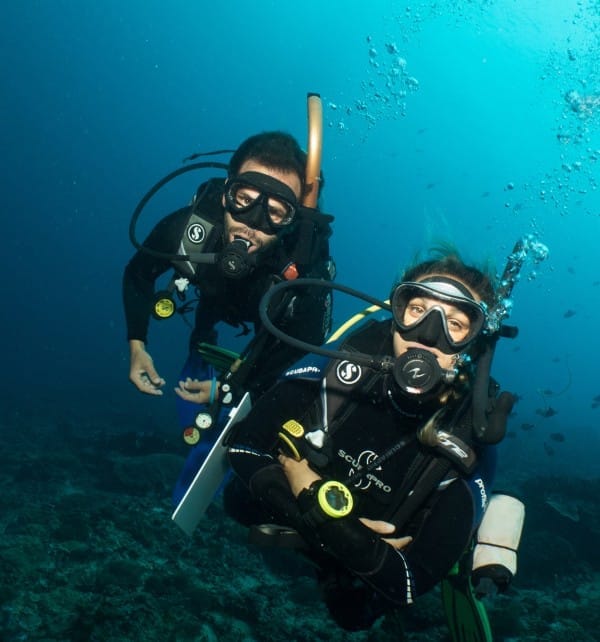 Two scuba divers exploring a coral seafloor off Nusa Lembongan, wearing full gear and breathing through regulators.