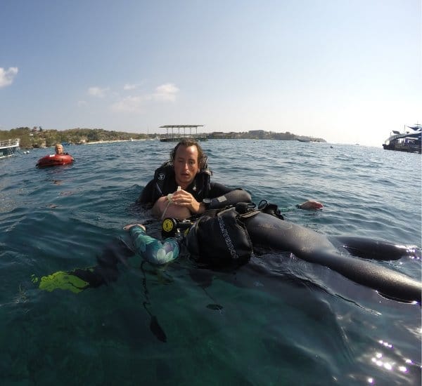 Scuba instructor supporting a diver floating face-up at the surface off Nusa Lembongan with boats nearby