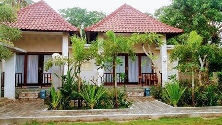 Two adjoining guest bungalows on Nusa Lembongan with shaded porches and wooden chairs amid tropical plants.