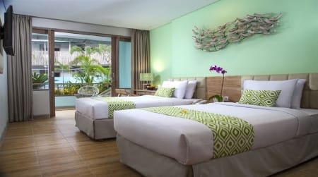 Two neat twin beds in a bright hotel room with green accent wall and balcony overlooking pool and palms on Nusa Lembongan