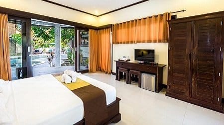 Bright Nusa Lembongan hotel room with neatly made bed, towel swans on bed and open glass doors leading to pool terrace.