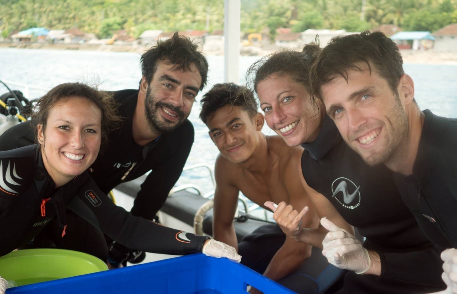 Five smiling divers posing with dive gear on a boat near Nusa Lembongan, leaning over a blue crate.