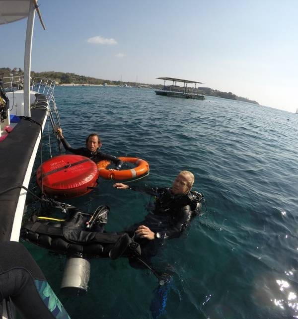 Decompress 1 Two scuba divers holding onto life buoys beside a boat while surfacing near Nusa Lembongan.