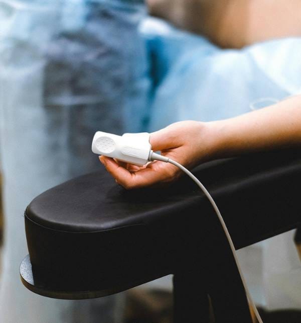 Decompress 3 Person in Nusa Lembongan resting an arm on an armrest while holding a finger pulse oximeter connected by a cable.