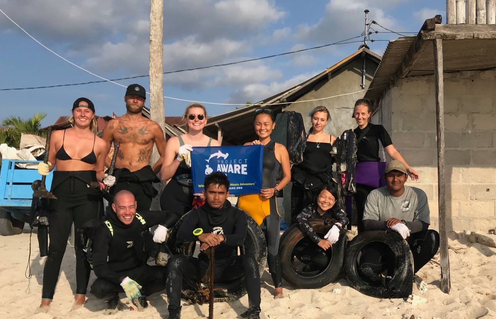 Volunteers on Nusa Lembongan beach pose with a Project AWARE banner and recovered tires and marine debris after a cleanup.