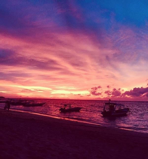 The experience of lifetime 2 Boats moored along the shore at Nusa Lembongan as a vivid pink and purple sunset reflects on the sea.