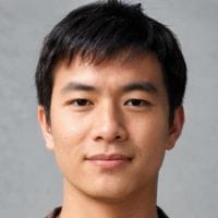 Young man with short dark hair and a slight smile facing the camera against a plain gray background.